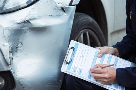 47932228-auto-workshop-mechanic-inspecting-damage-to-car-and-filling-in-repair-estimate